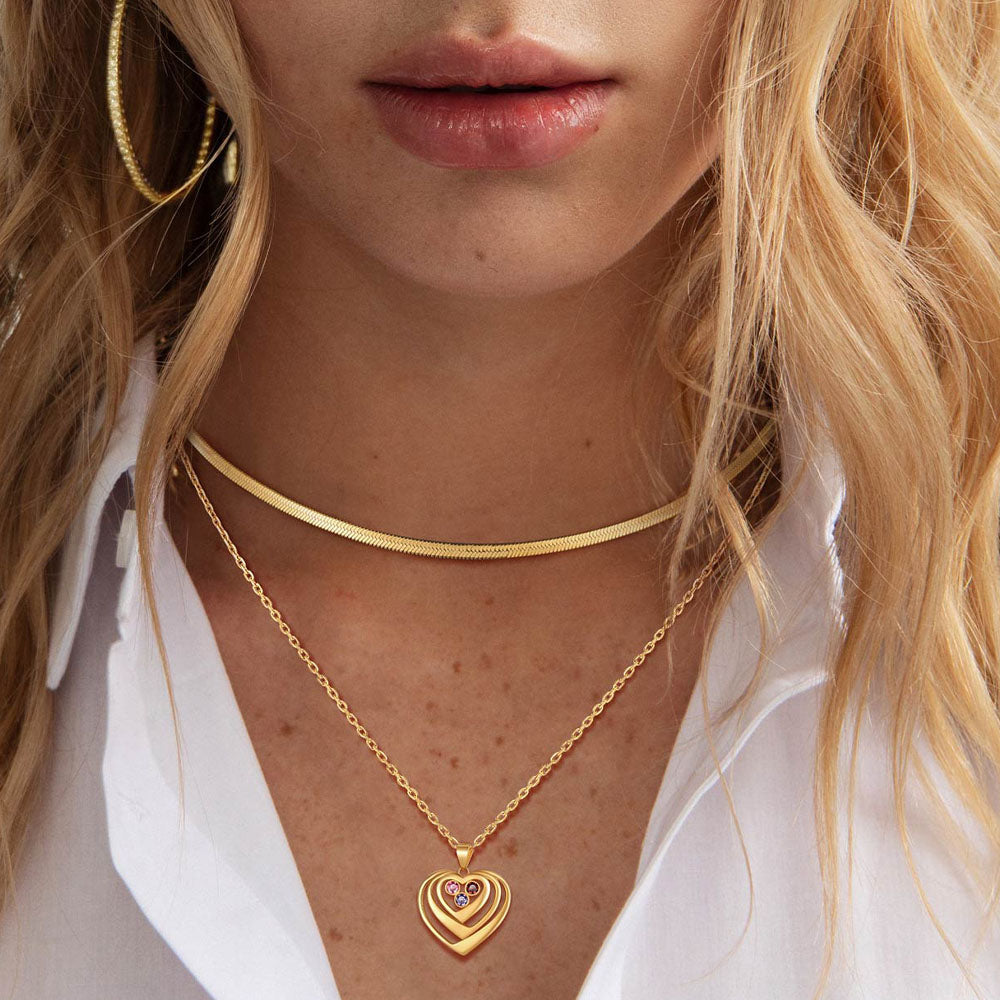 Close-up of a person wearing a gold heart-shaped birthstone necklace with a white shirt.