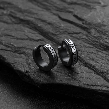 Black hoop earrings with viking rune on a dark stone surface