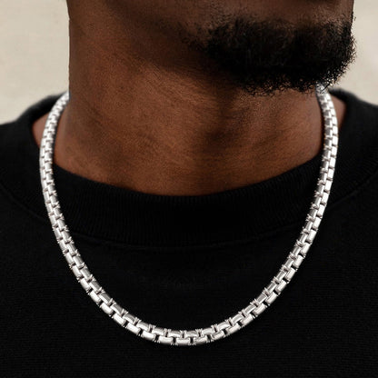 Silver chain necklace worn by a person on a black background