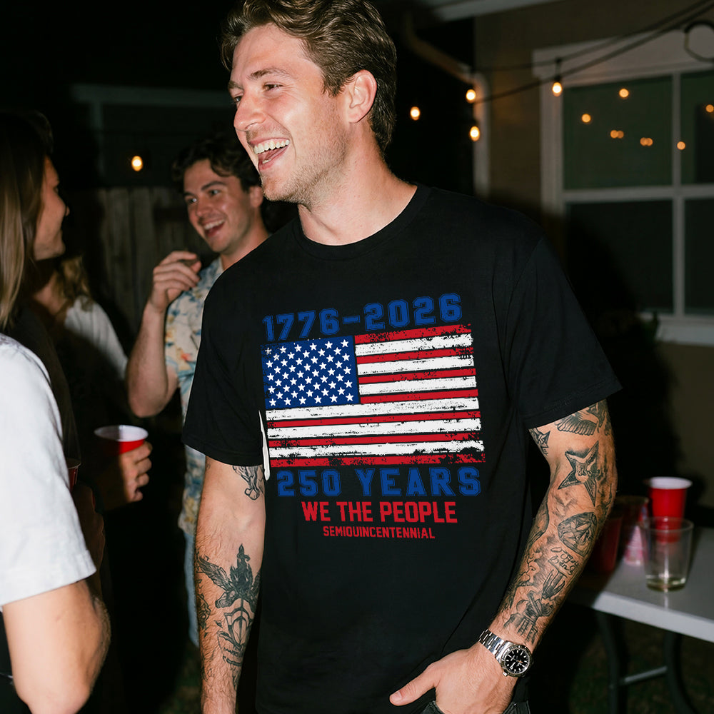 Man wearing a black t-shirt with an American flag design and text, standing in a social setting.