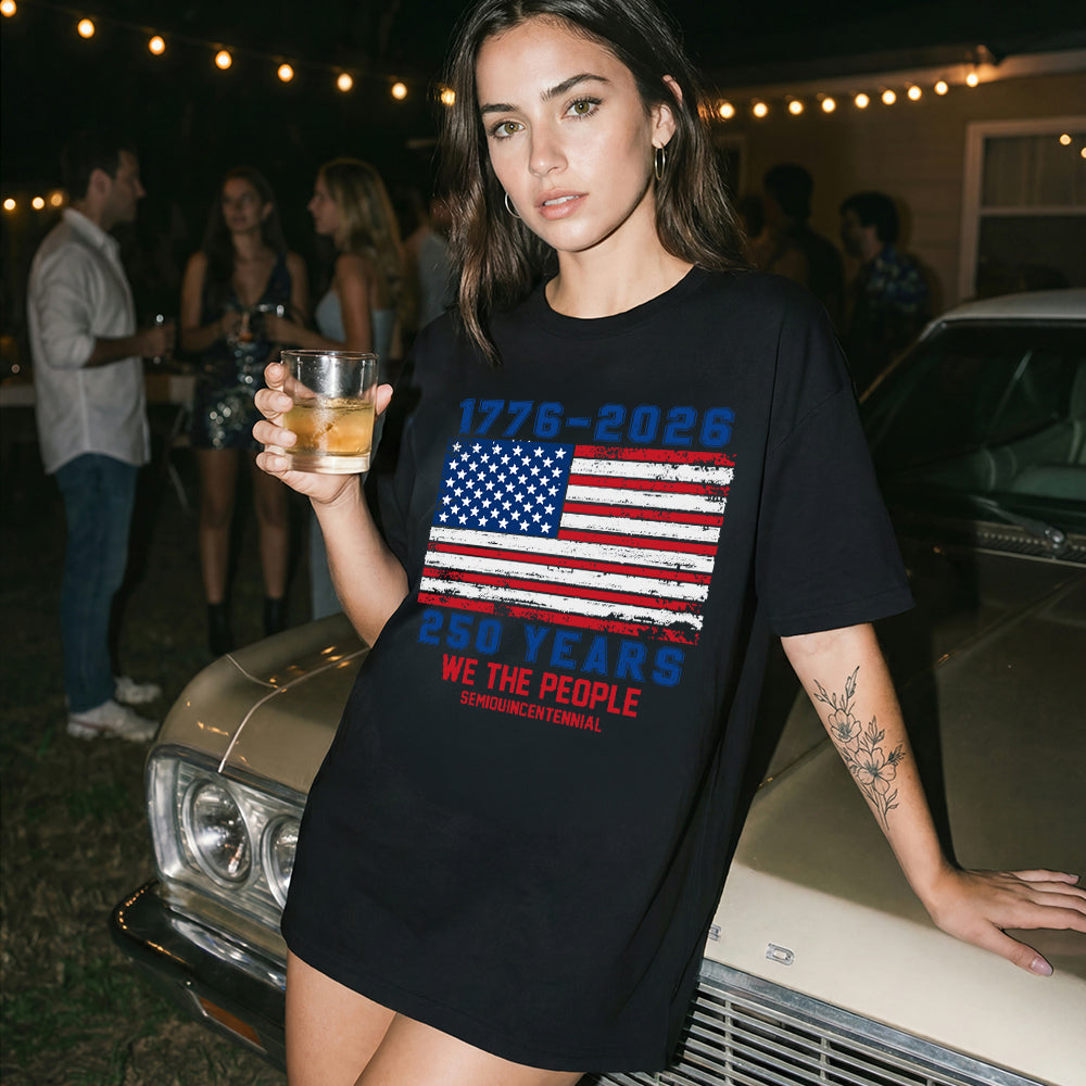 Woman wearing a black t-shirt with an American flag design, holding a drink, standing next to a vintage car at a party.