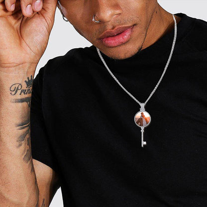 Person wearing a black shirt with a key-shaped pendant necklace featuring an image of two people.