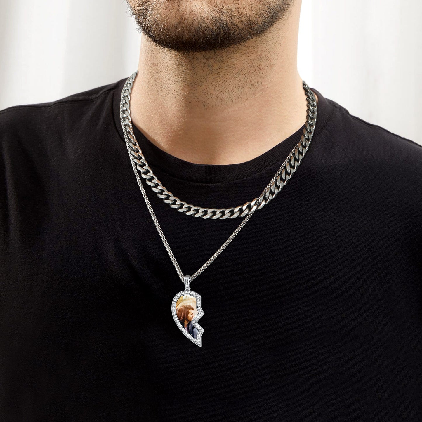 Man wearing a black shirt with a silver chain necklace featuring a pendant.
