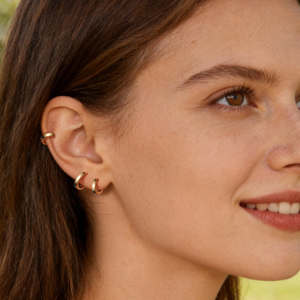 Woman wearing gold hoop earrings with a blurred outdoor background
