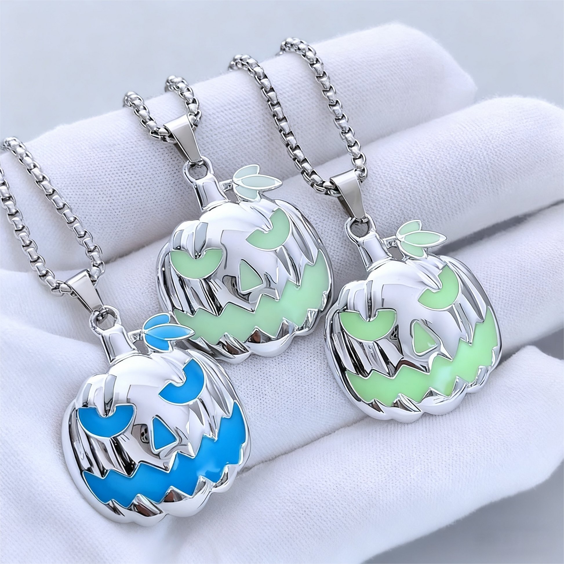 Three silver pumpkin-shaped pendants with glowing blue and green faces on a white surface.