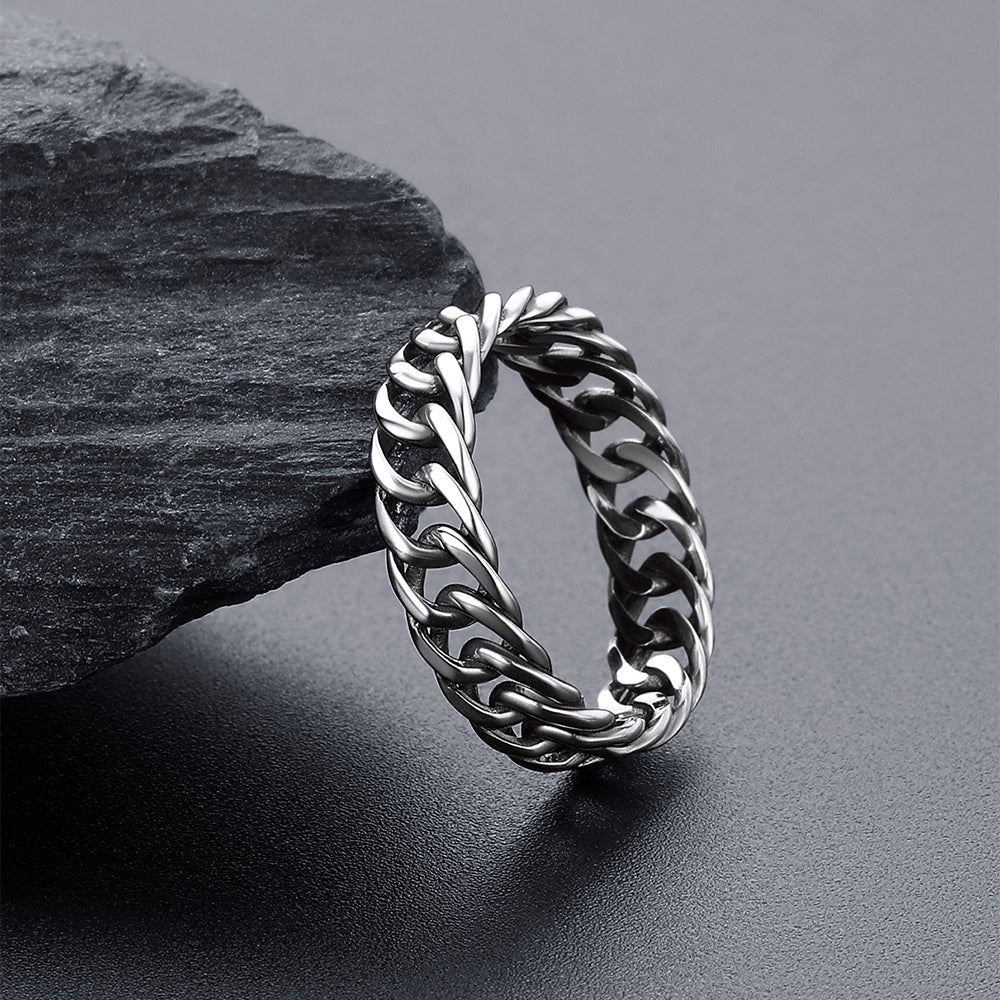 A silver-toned chunky chain-link ring resting on a dark gray surface .