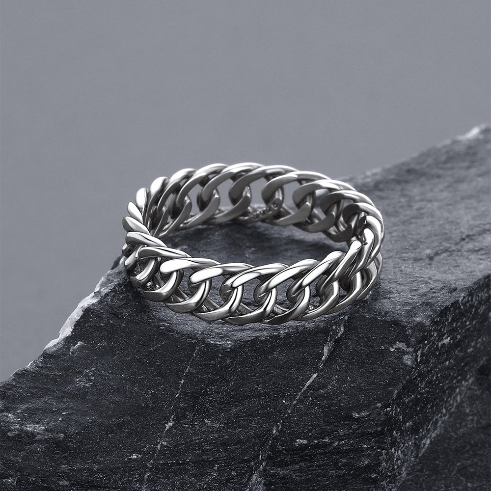 A silver-tone curb link ring resting on a dark textured slate surface against a neutral gray background.