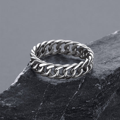 A silver-tone curb link ring resting on a dark textured slate surface against a neutral gray background.