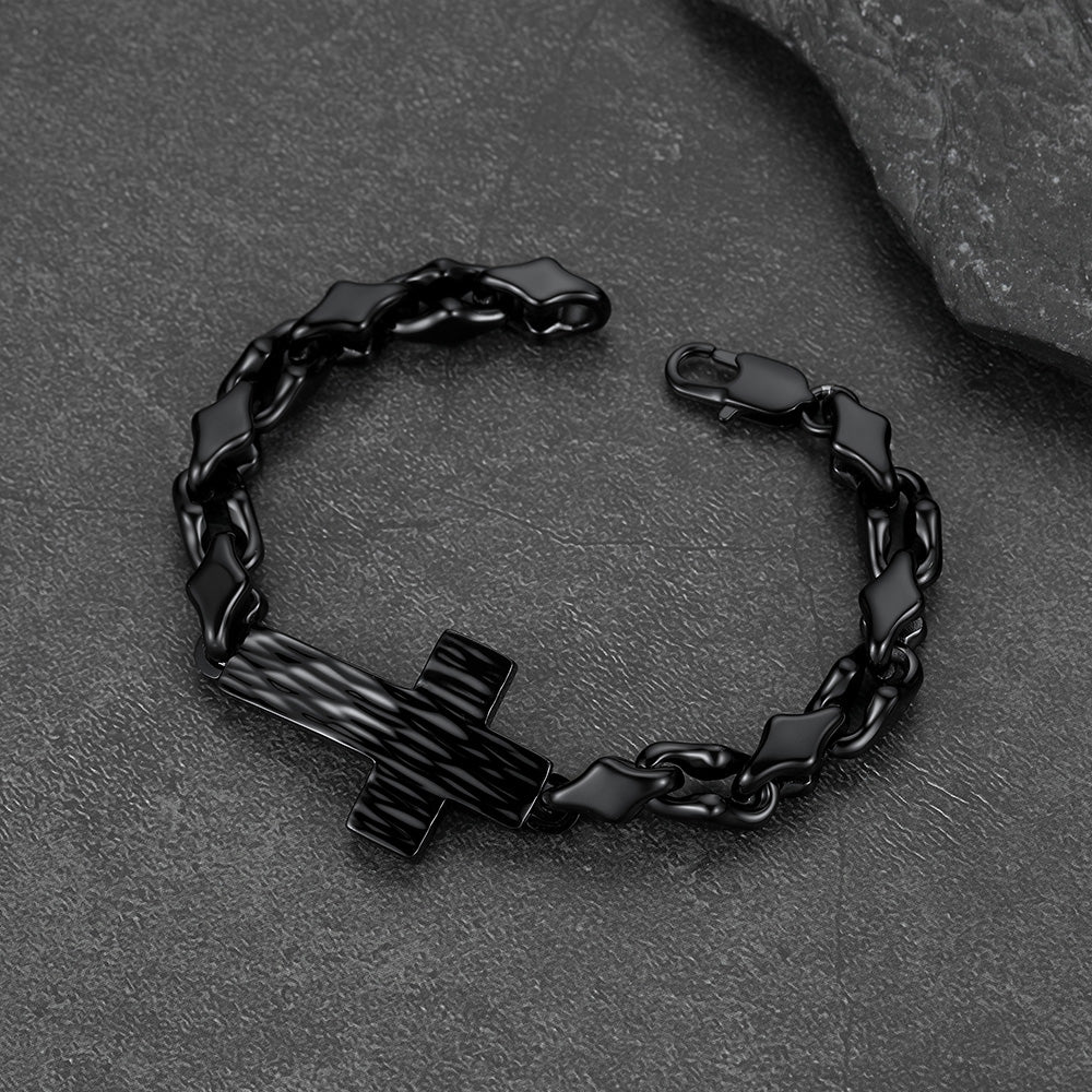 A black metal chain bracelet with a cross-shaped centerpiece, photographed on a dark textured stone surface.