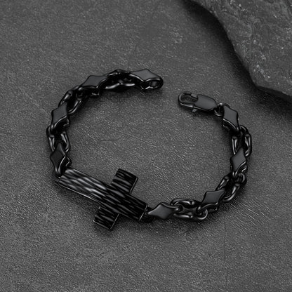 A black metal chain bracelet with a cross-shaped centerpiece, photographed on a dark textured stone surface.