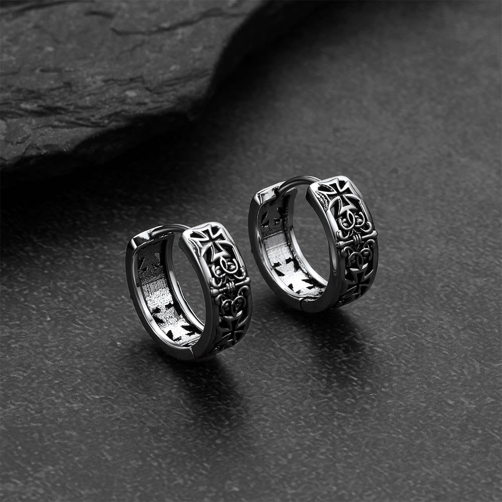 Pair of silver hoop earrings with cross designs on a dark surface