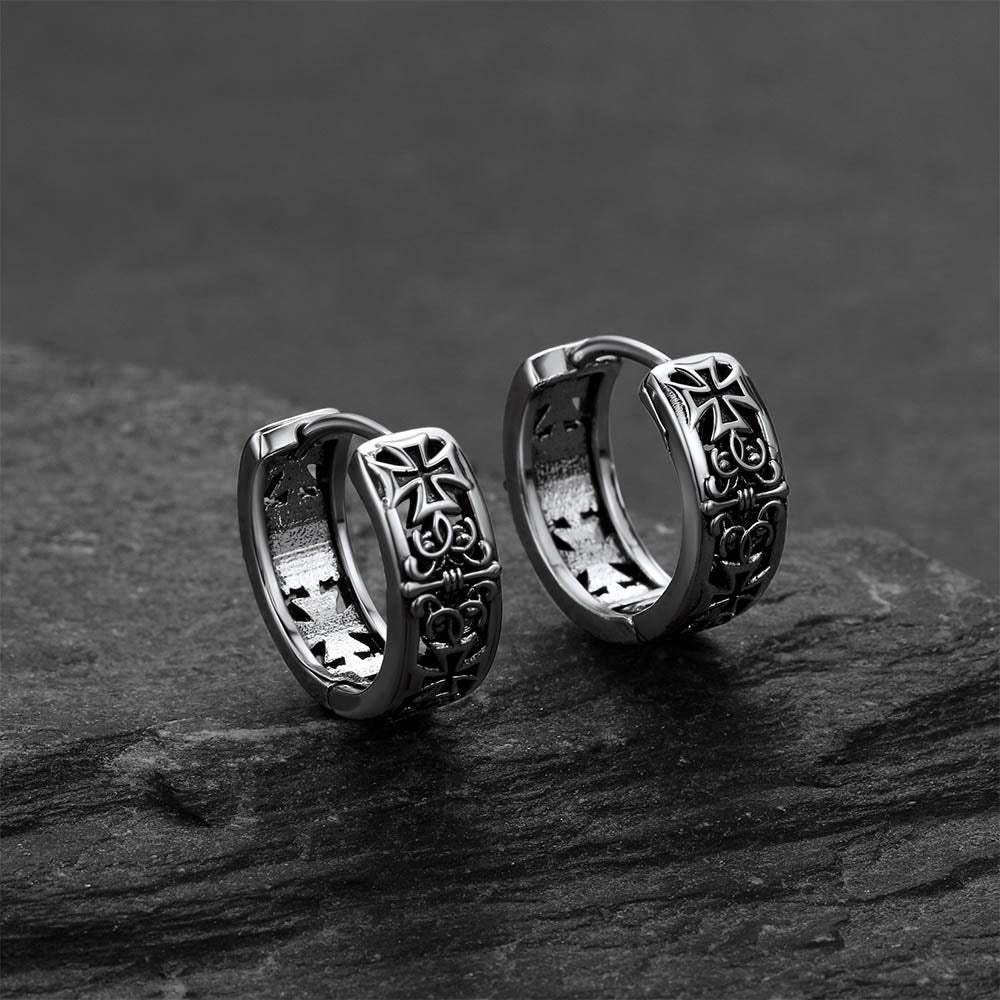 Pair of silver hoop earrings with cross designs on a dark stone surface.