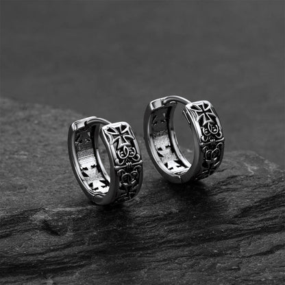 Pair of silver hoop earrings with cross designs on a dark stone surface.