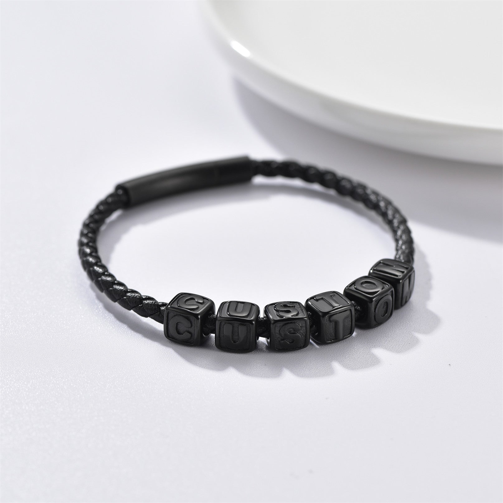 Black braided bracelet with lettered beads on a white background
