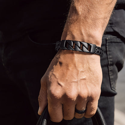 Person holding a black leather bag with a close-up of their arm wearing a black bracelet.