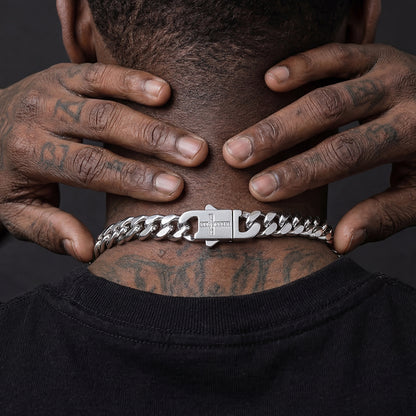 Person wearing a silver chain necklace with tattoos on neck and hands against a dark background