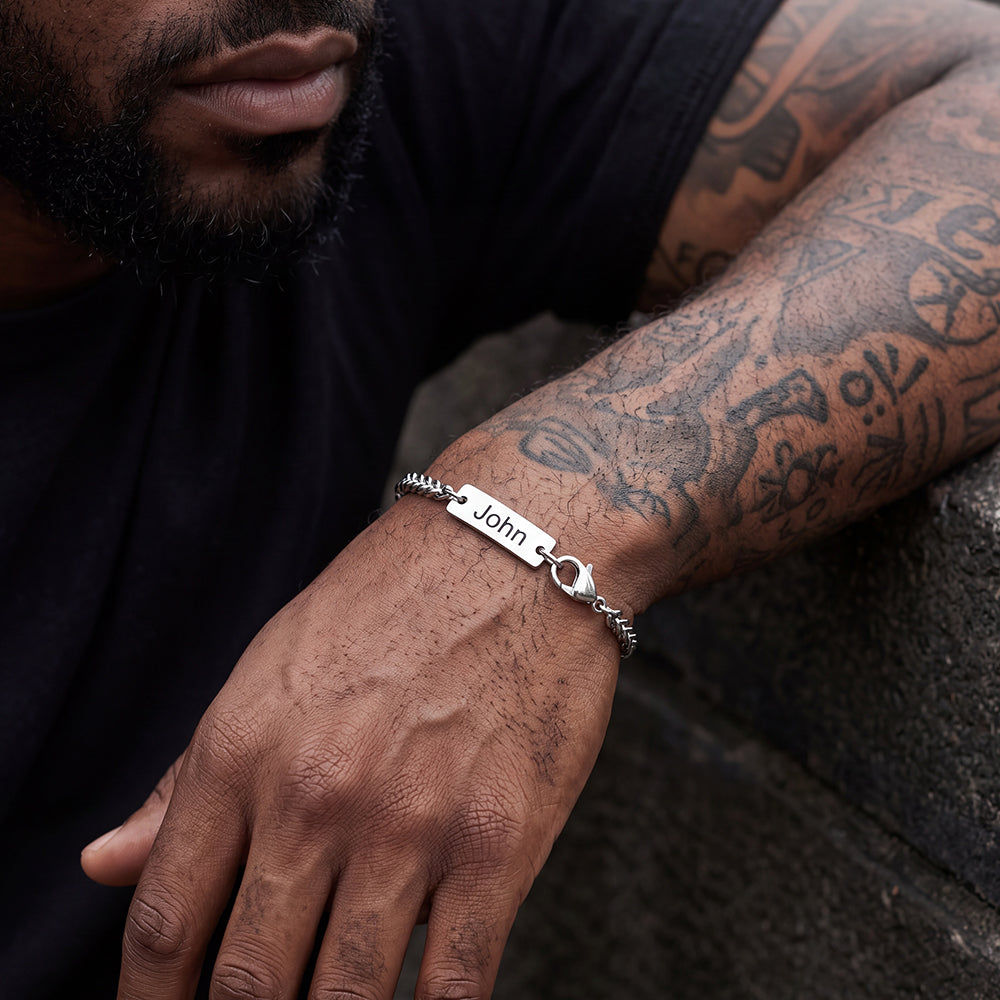 A  man wearing a silver chain bracelet with a rectangular nameplate.