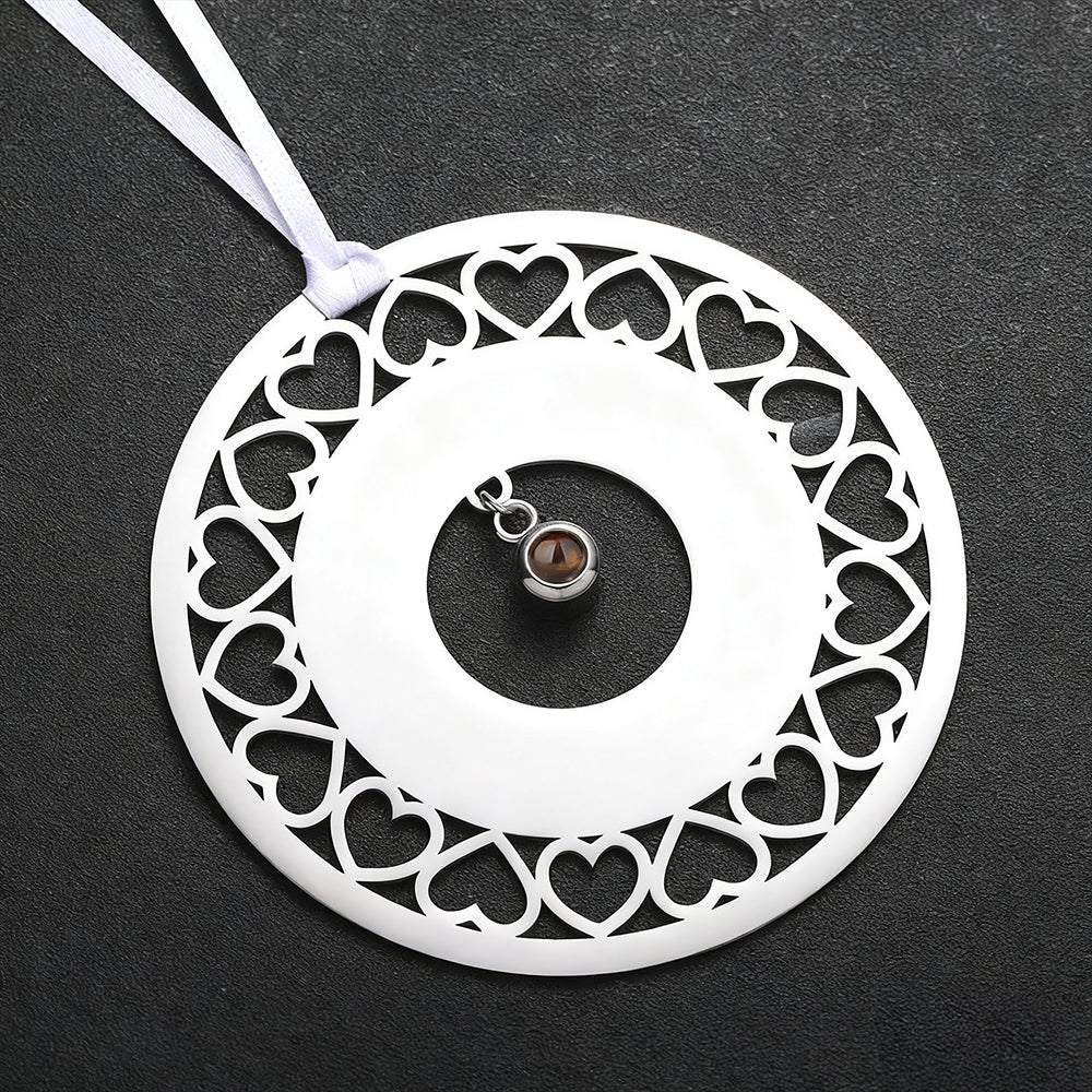 Decorative white circular ornament with heart patterns and a small brown gemstone on a dark background.