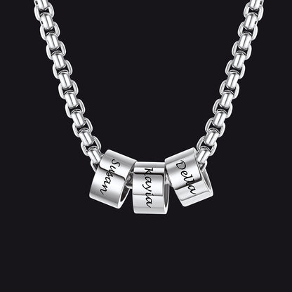 Silver necklace with three engraved cylindrical pendants on a black background