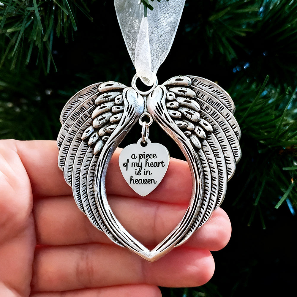 Silver angel wing ornament with heart pendant held against a green background