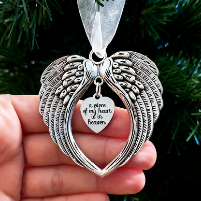 Silver angel wing ornament with heart pendant held against a green background