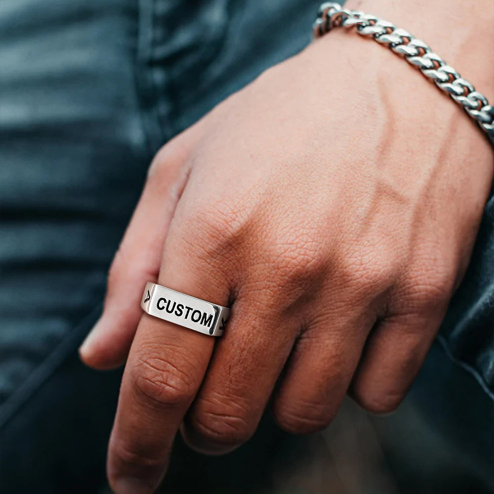 Hand wearing a silver ring with 'CUSTOM' engraving, blurred background