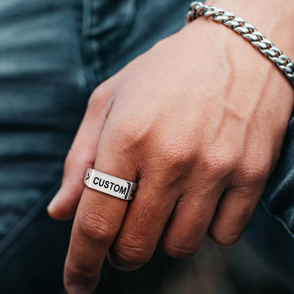 Hand wearing a silver ring with 'CUSTOM' engraving, blurred background