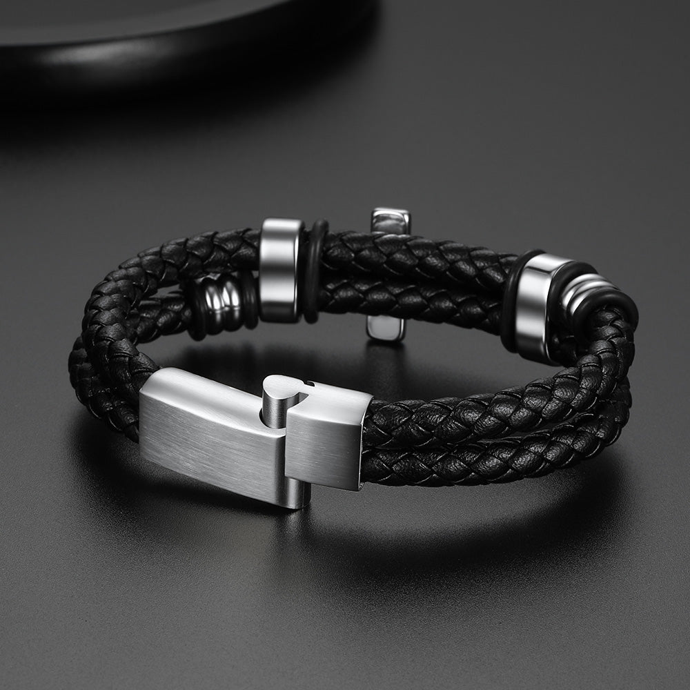 A men's braided leather bracelet with a brushed silver-tone metal clasp and matching silver spacer beads, displayed on a dark gray surface.