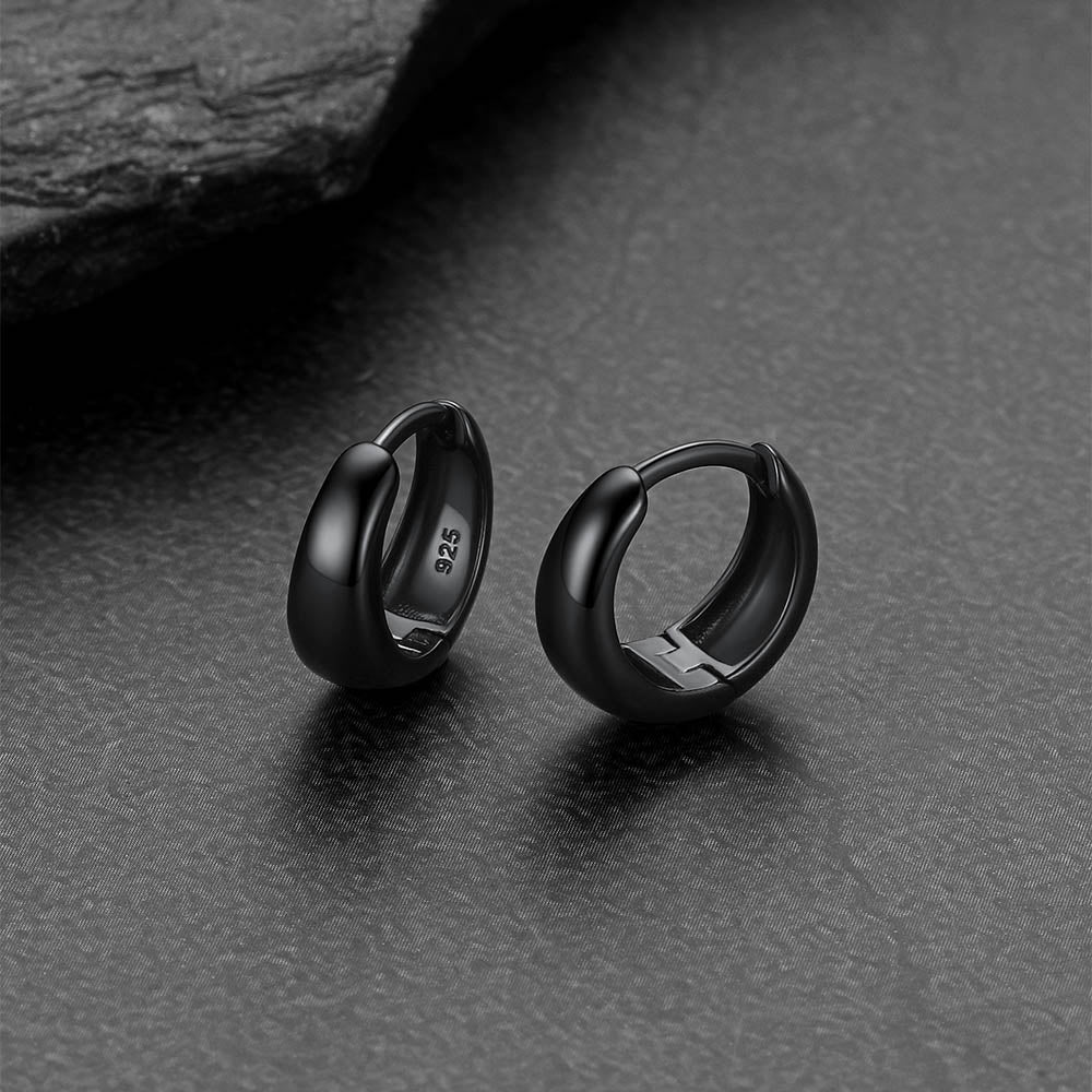 Black hoop earrings on a dark textured surface