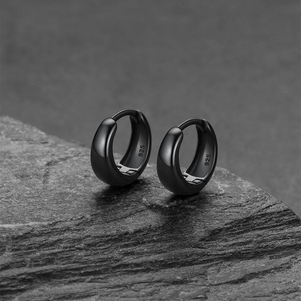 Black hoop earrings on a dark stone surface with a gray background