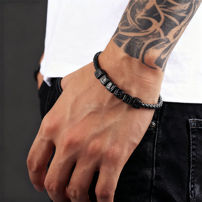 Black braided bracelet on a wrist with tattoos against a neutral background