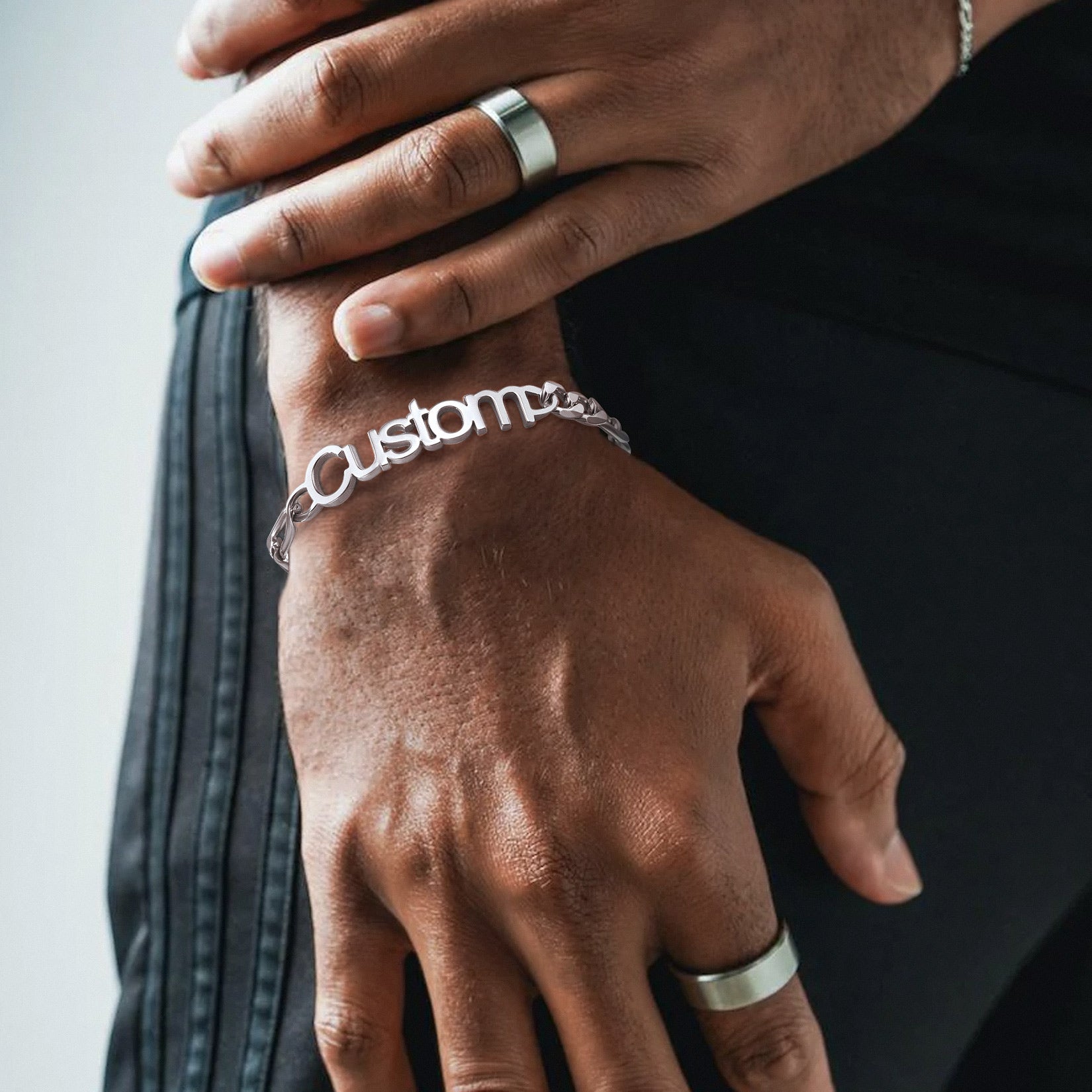 Close-up of a hand wearing a silver bracelet with 'custom' engraved on it.
