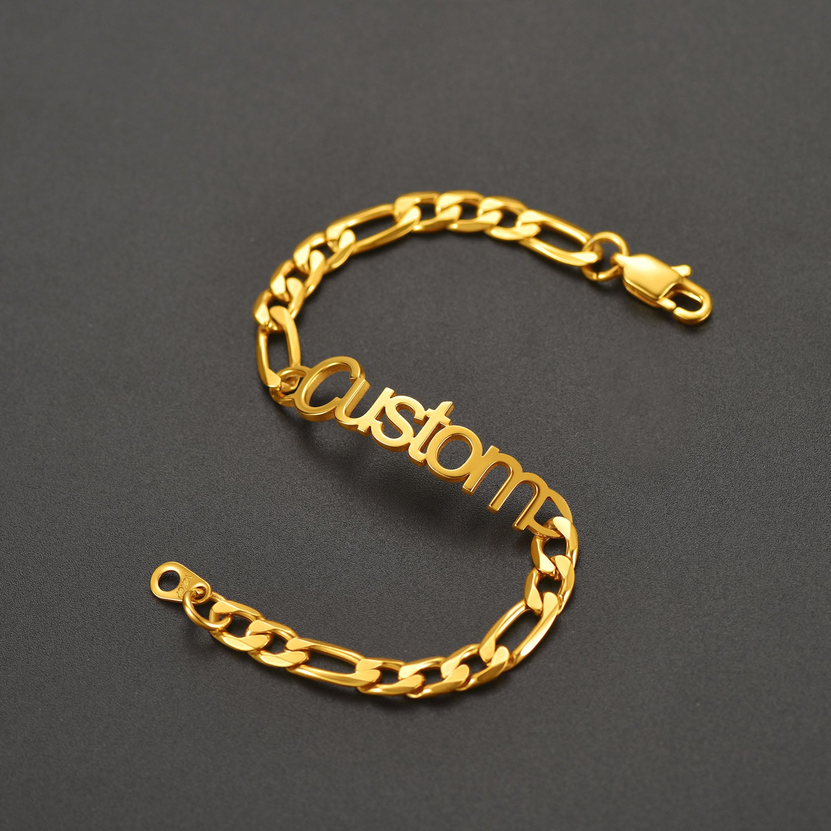 Gold chain bracelet with 'custom' engraving on a dark gray background