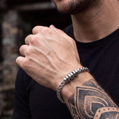 A close-up of a man's wearing a silver-toned chain bracelet with engraved lettering.