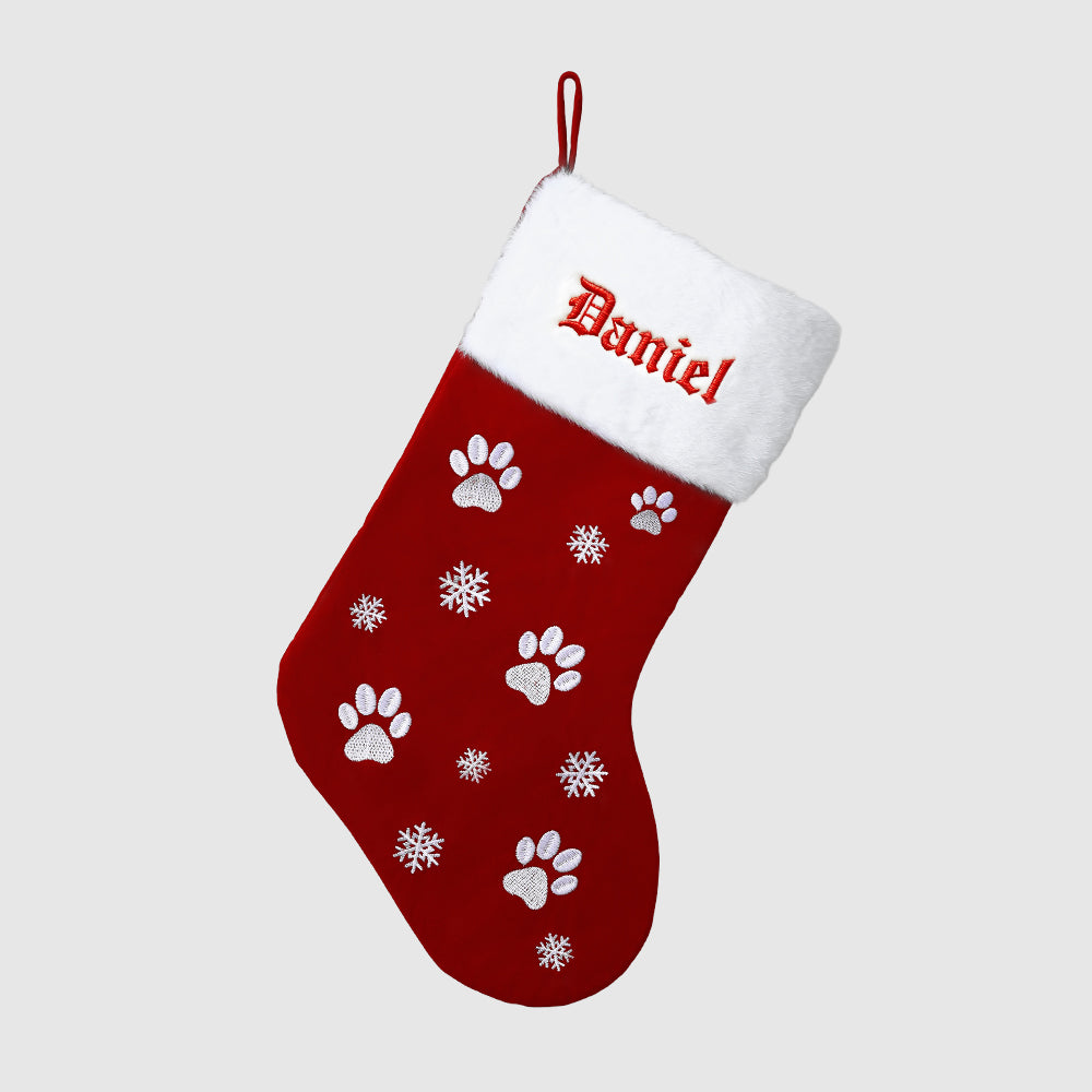 Red Christmas stocking with white paw prints and snowflakes, personalized with 'Daniel'.