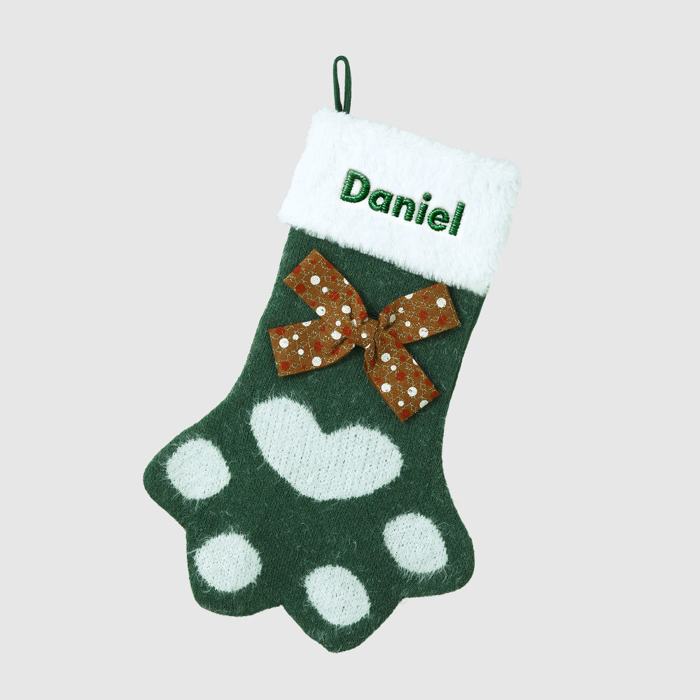 Green paw print stocking with a brown bow and 'Daniel' embroidered on a light gray background
