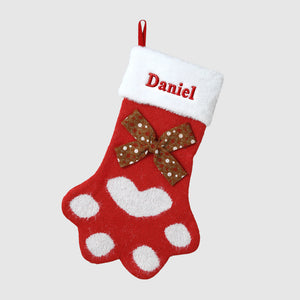 Red Christmas stocking with white paw prints and a brown bow, personalized with 'Daniel'.