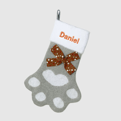 Gray paw print stocking with a brown bow and 'Daniel' text on a white background