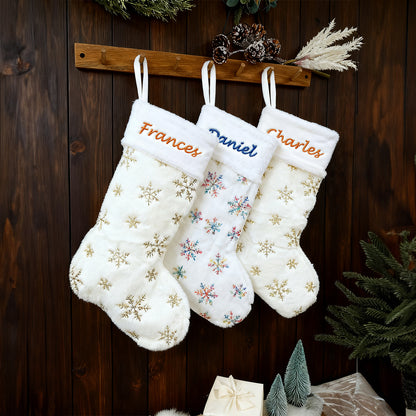 Three white Christmas stockings with embroidered names hanging on a wooden rack against a dark wood background.