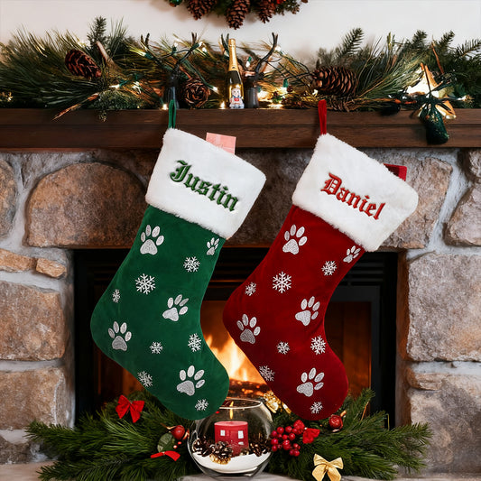 Two Christmas stockings, one green and one red, with names embroidered on them, hanging by a fireplace.img