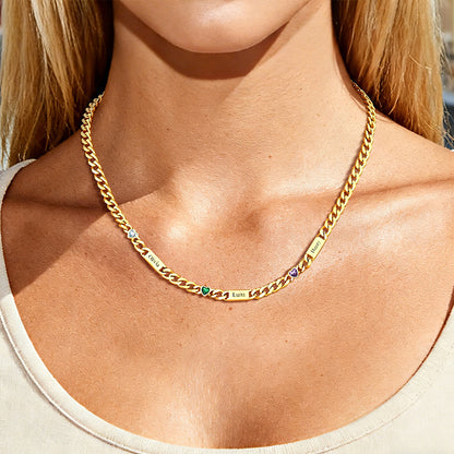 Gold chain necklace with engraved names on a person wearing a beige top.