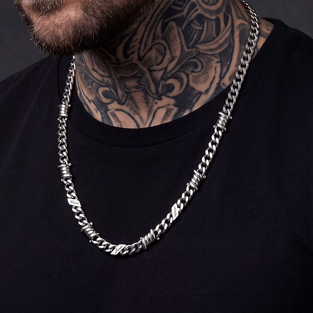 A close-up of a man wearing a thick silver-toned chain necklace with textured, twisted barbed wire details.