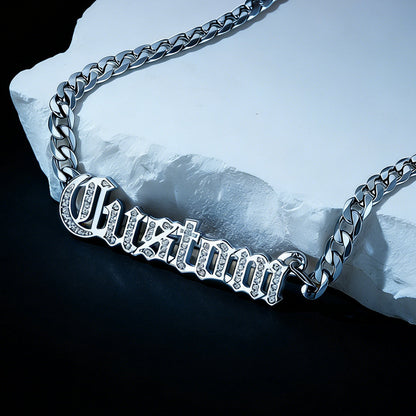 Silver chain necklace with 'Custom' engraving on a stone surface