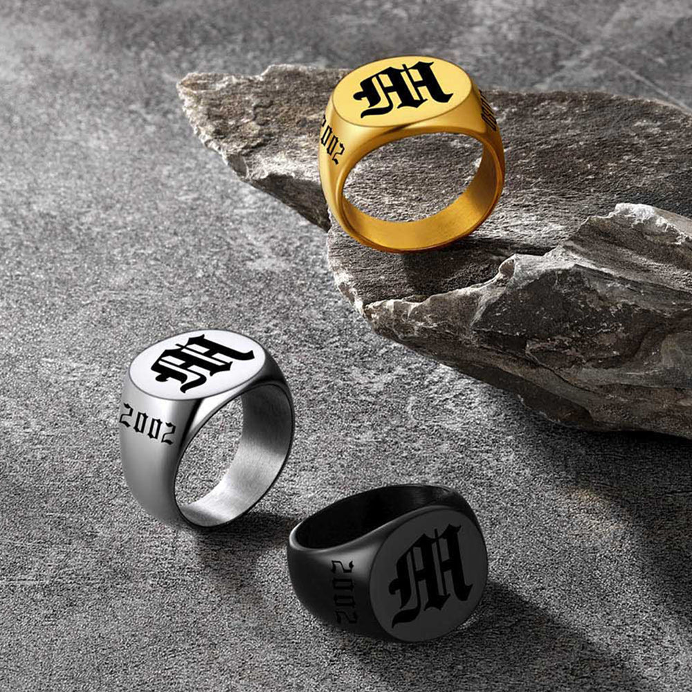 Three rings in gold, silver, and black on a textured stone surface.