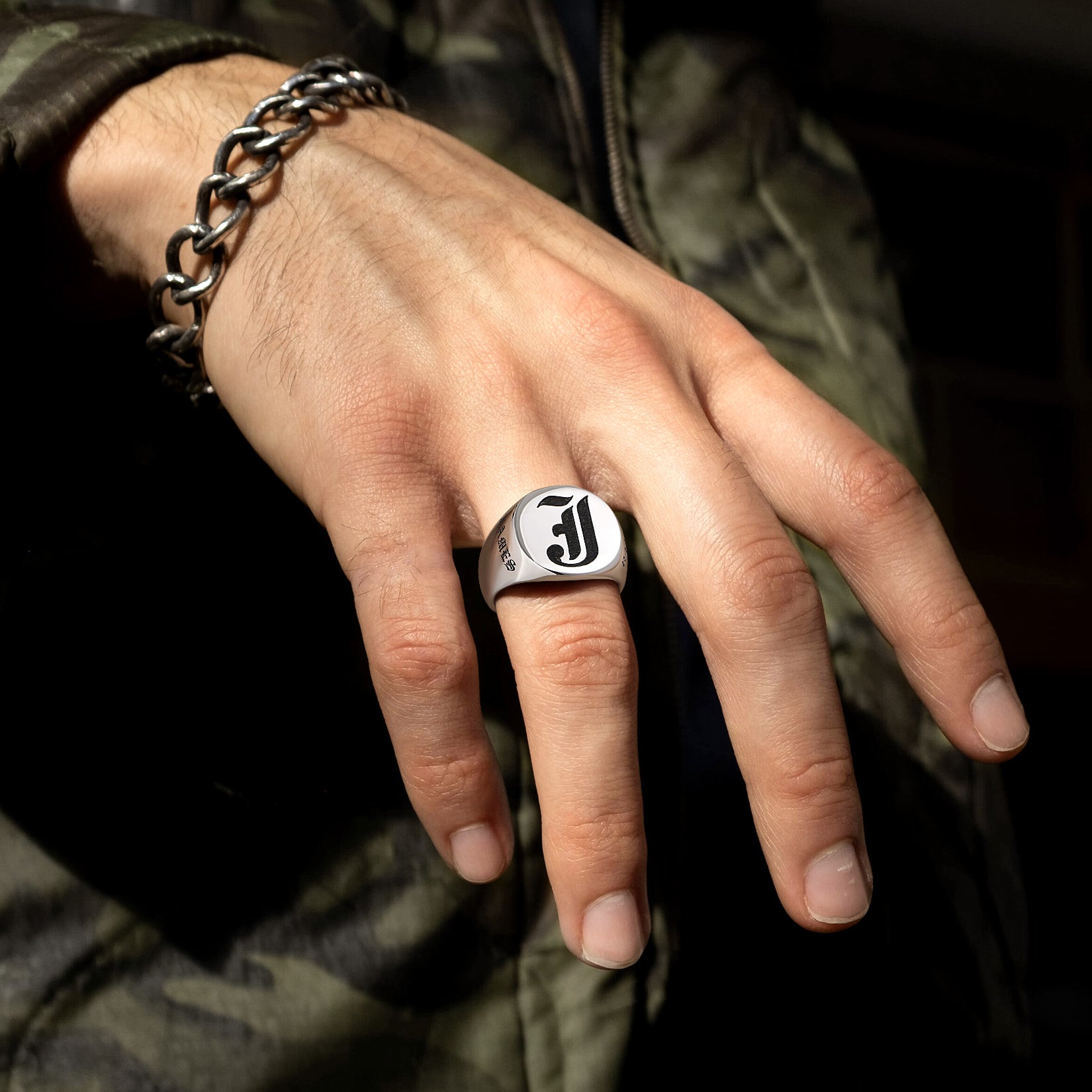 Hand wearing a silver ring with a logo, set against a dark background