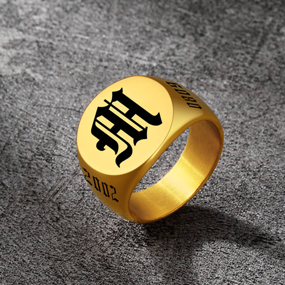 Gold ring with black engraved design on a textured gray surface