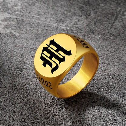 Gold ring with black engraved design on a textured gray surface