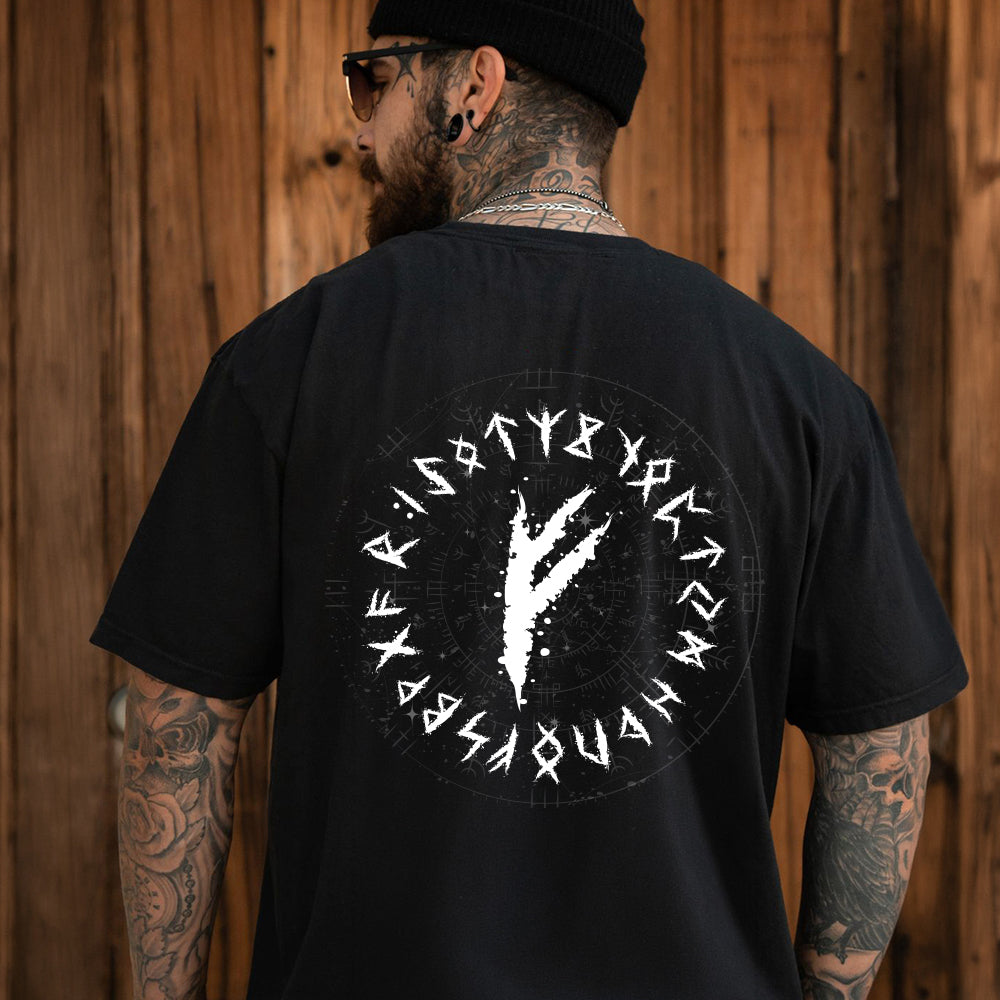 Man wearing a black t-shirt with a white viking rune on the back, standing against a wooden wall.