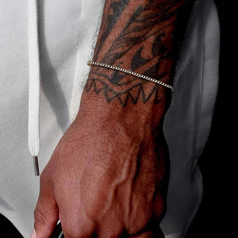 Hand with a tattoo and chain bracelet against a light background