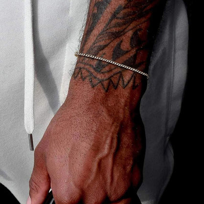 Hand with a tattoo and chain bracelet against a light background